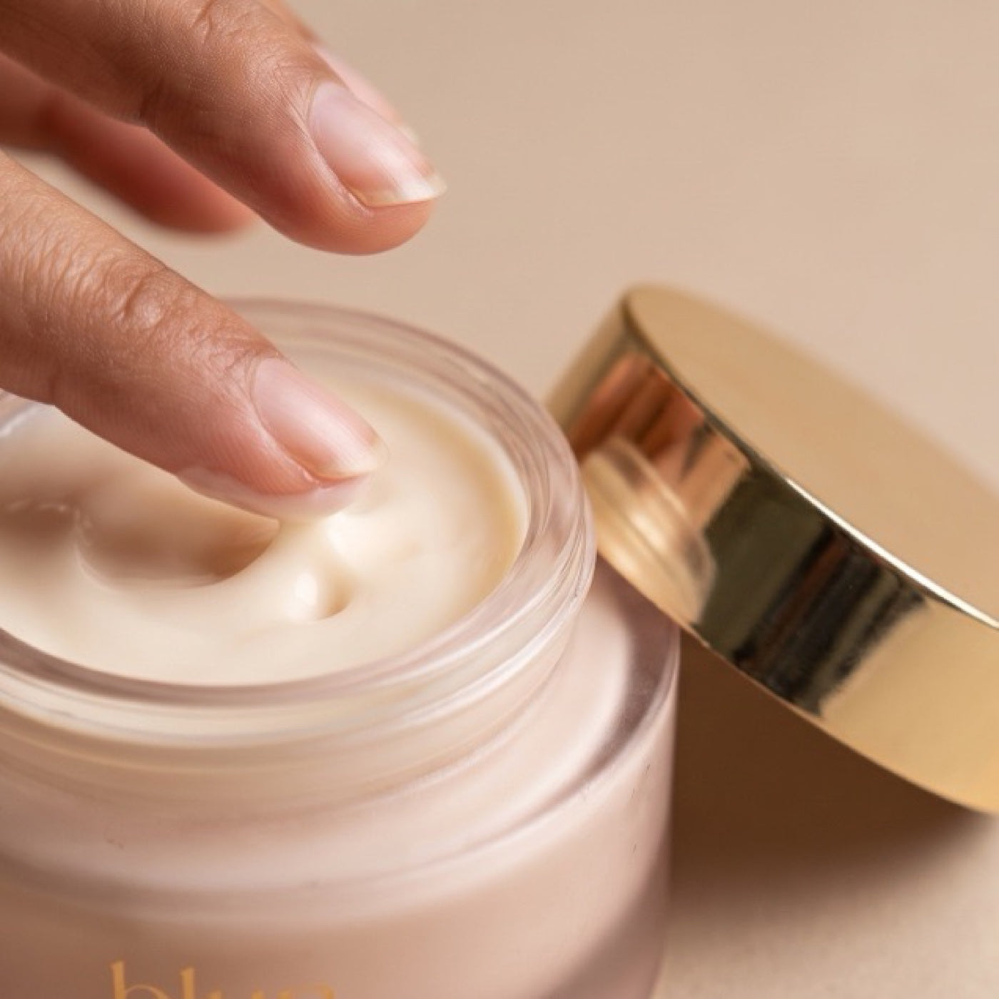 Close-up of Blun Camel Milk Cream texture on a fingertip, a light ivory emulsion